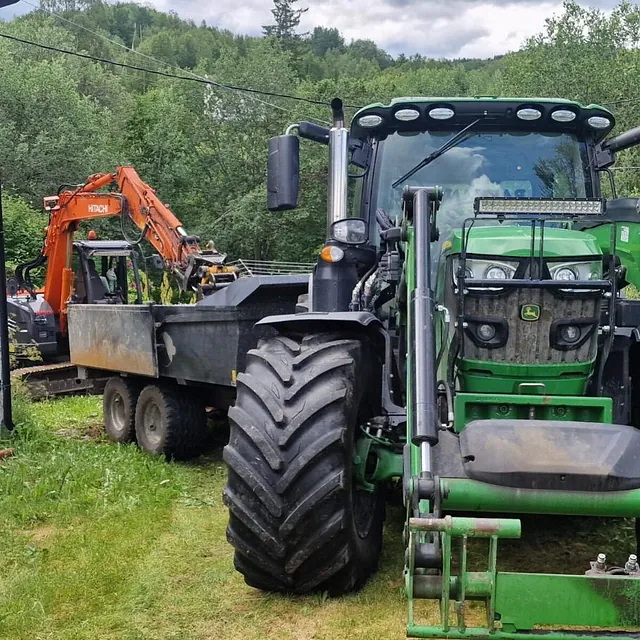 Traktor og gravemaskin ved bolig, klare for transport og grunnarbeid på eiendom